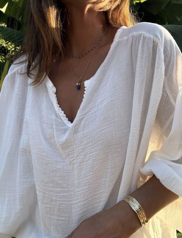 Blouse Agathe – Voile de Coton Blanc La blouse Agathe blanche est une pièce fluide et féminine à avoir dans sa garde-robe. Son voile de coton léger assure confort et élégance. Elle présente une coupe oversize flatteuse et un col V orné de dentelle, pour une touche romantique. Les manches 3/4, finies par un élastique discret, ajoutent de la souplesse au mouvement. La taille unique convient aux morphologies du 38 au 44. Fabriquée avec soin en Italie, cette blouse allie qualité et légèreté. Coloris : blanc Matière : voile de coton Col V avec finition dentelle Manches trois quarts avec élastique Coupe oversize Taille unique : convient du 38 au 44 Fabriquée en Italie