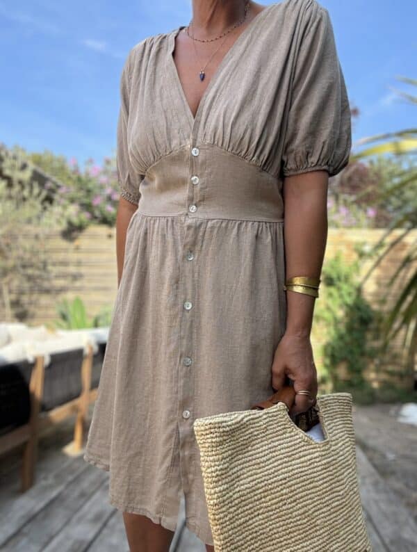 Robe mi-longue Soline – Coloris camel Voici la robe Soline en camel, une teinte chaude et naturelle qui sublime la silhouette avec élégance. Composition fluide : viscose & lin Décolleté plongeant délicat Fermeture sur le devant avec boutons nacrés Manches courtes finies par un élastique léger Coupe mi-longue flatteuse et fluide Élastique souple au dos pour plus d’aisance Découpe légèrement plus ample sur le ventre Coloris camel facile à porter et associer Taille unique (du 36 au 40) Confection italienne Parfait avec des sandales dorées, un panier et un chapeau de paille pour un look 100 % bohème-chic.