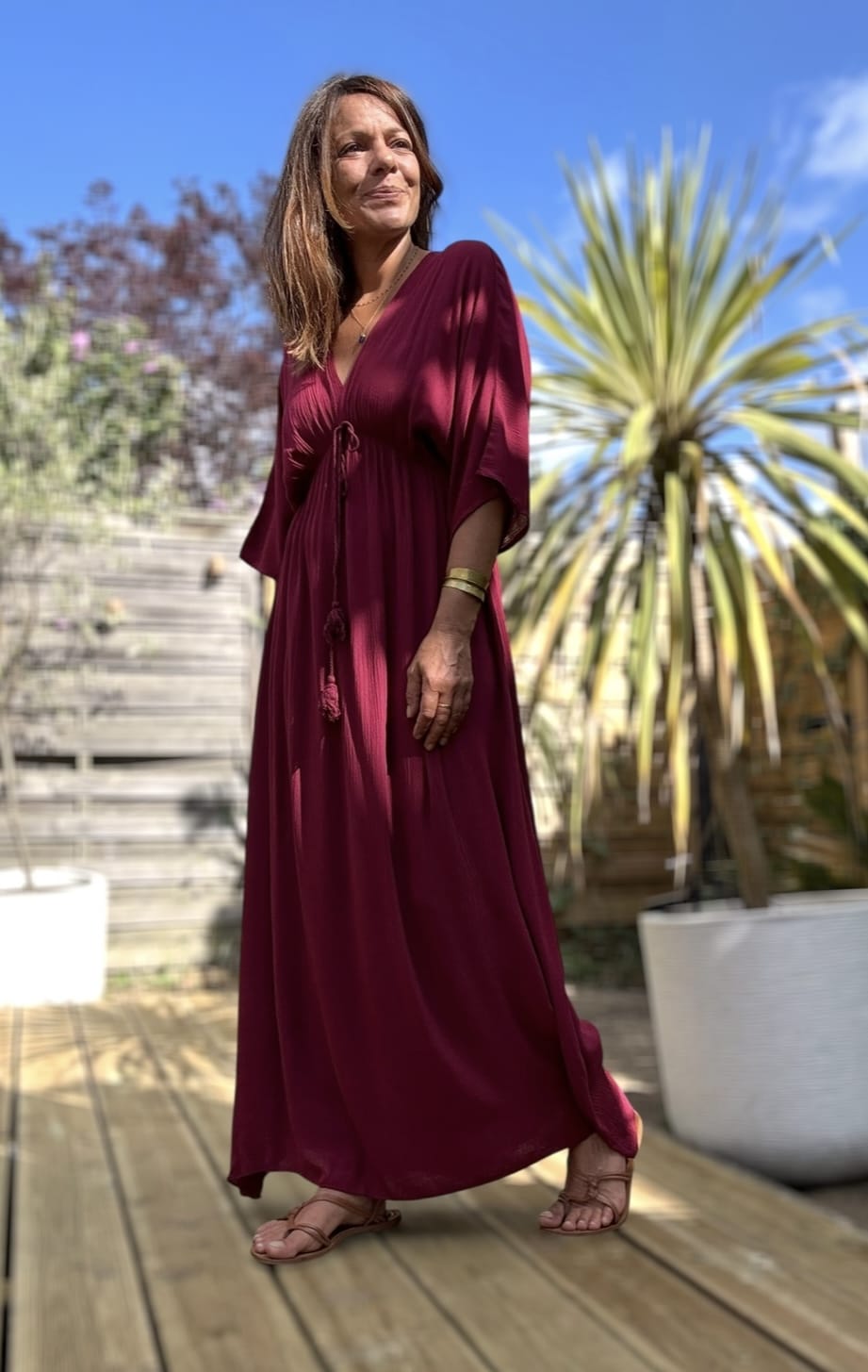 Robe longue fluide bordeaux – LENAE Découvrez la robe LENAE bordeaux, longue et fluide, au tombé naturel et à la couleur profonde. Elle met en valeur chaque silhouette avec douceur et élégance. Sa matière en viscose assure confort, légèreté et fluidité. Elle est idéale pour l'été ou la mi-saison. Le décolleté en V devant et au dos structure la robe avec féminité. L'élasticité fine sous la poitrine souligne subtilement la taille. Un lien à nouer, terminé par de jolis pompons, permet d’ajuster la coupe selon vos envies. Couleur : bordeaux Matière : viscose légère Décolleté : devant et dos Manches : courtes Ceinture : lien à pompons Coupe : droite, légèrement évasée Taille : unique (36 à 40) Fabrication : Italie Associez-la à des accessoires dorés, à une veste en jean ou un gilet léger pour les soirées d'été. LENAE prune, c’est la robe parfaite pour les beaux jours, les soirées, et les instants qui comptent. Edition limitée – dernière chance !