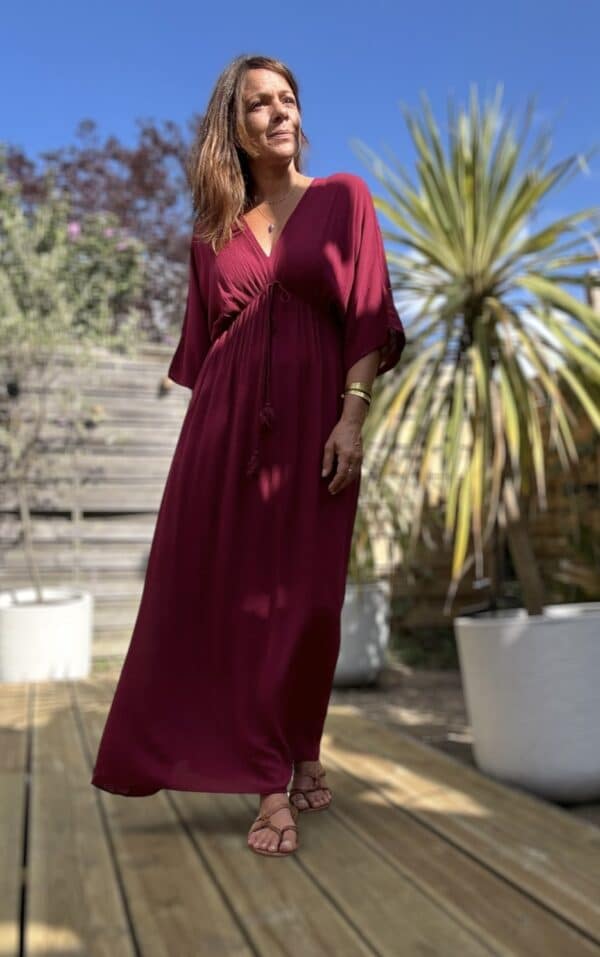 Robe longue fluide bordeaux – LENAE Découvrez la robe LENAE bordeaux, longue et fluide, au tombé naturel et à la couleur profonde. Elle met en valeur chaque silhouette avec douceur et élégance. Sa matière en viscose assure confort, légèreté et fluidité. Elle est idéale pour l'été ou la mi-saison. Le décolleté en V devant et au dos structure la robe avec féminité. L'élasticité fine sous la poitrine souligne subtilement la taille. Un lien à nouer, terminé par de jolis pompons, permet d’ajuster la coupe selon vos envies. Couleur : bordeaux Matière : viscose légère Décolleté : devant et dos Manches : courtes Ceinture : lien à pompons Coupe : droite, légèrement évasée Taille : unique (36 à 40) Fabrication : Italie Associez-la à des accessoires dorés, à une veste en jean ou un gilet léger pour les soirées d'été. LENAE prune, c’est la robe parfaite pour les beaux jours, les soirées, et les instants qui comptent. Edition limitée – dernière chance !