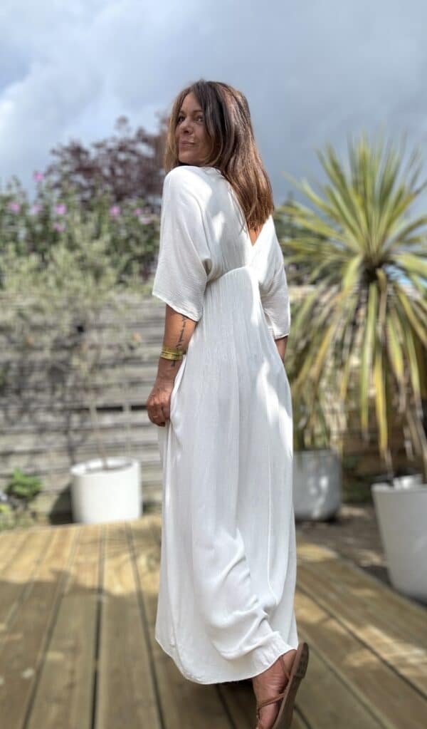 Robe longue fluide écrue – LENAE La robe LENAE écrue séduit par sa coupe longue, fluide et féminine. Elle offre un tomber naturel, parfait en toute occasion. Confectionnée en viscose légère, elle est agréable à porter même en plein été. Sa matière douce épouse les mouvements sans coller à la peau. Le décolleté en V se retrouve à l’avant comme à l’arrière, pour une touche féminine subtile. Sous la poitrine, un élastique fin souligne la taille sans comprimer. Un lien à nouer, orné de pompons, permet d’ajuster la robe avec charme et confort. Matière : viscose fluide Couleur : écrue Décolleté : devant et dos Manches : courtes Ceinture : lien à pompons Coupe : droite et évasée Taille : unique (36 à 40) Fabrication : Italie Associez-la à des sandales ou des espadrilles pour un look estival chic. Portez-la aussi en soirée avec une veste légère. ✨ Une robe pour briller au soleil, bouger librement, et se sentir belle en un clin d’œil. Attention : quantité très limitée !