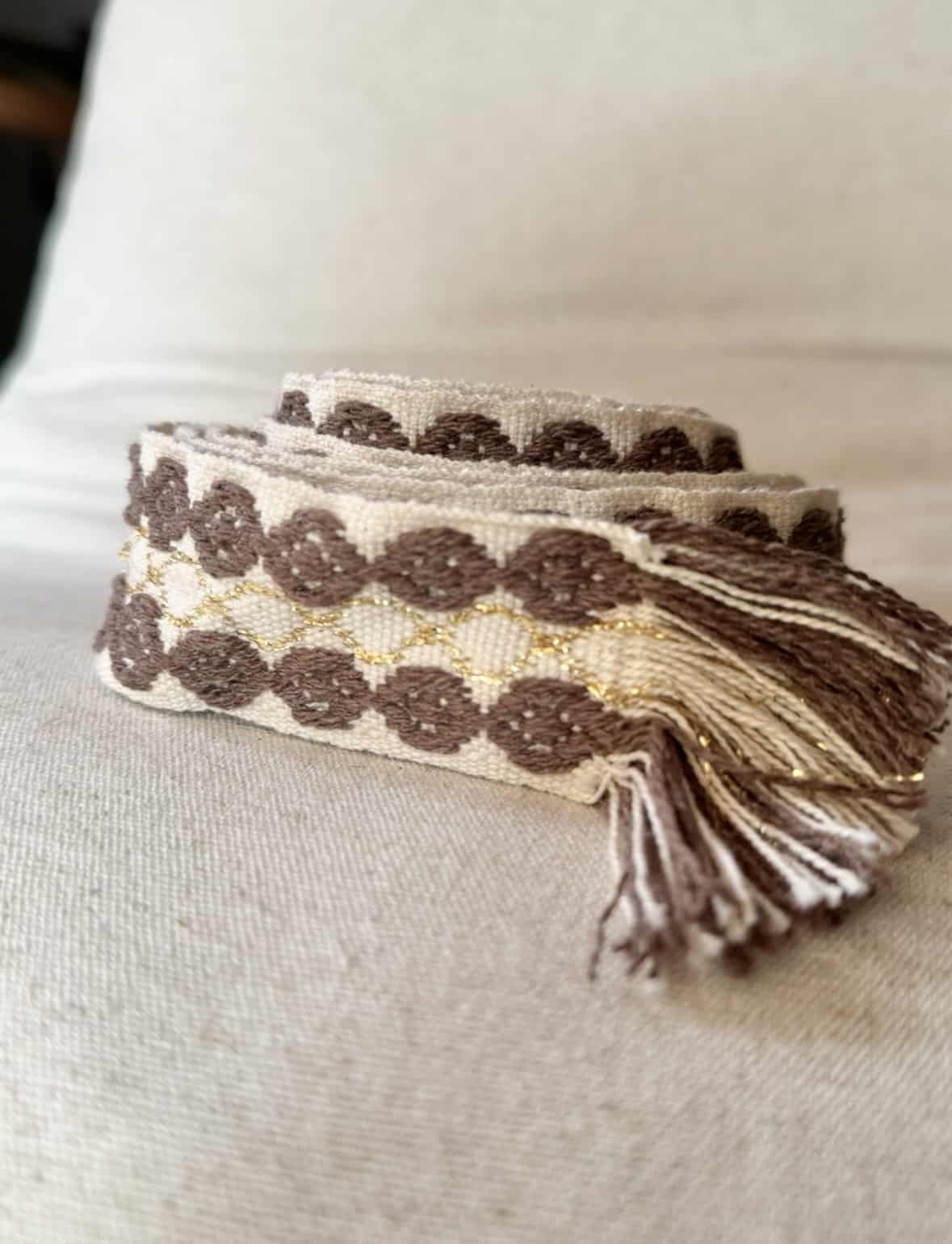 L’accessoire bohème chic par excellence La ceinture POLIG incarne l’élégance décontractée du style bohème chic. Confectionnée en coton doux, elle offre à la fois souplesse, texture et charme artisanal. Ses motifs ronds brodés couleur chocolat rappellent le travail soigné des pièces faites à la main. Le liseré doré apporte une touche de lumière et de féminité, idéale pour rehausser vos tenues. Grâce à sa matière naturelle, la ceinture POLIG reste agréable et facile à ajuster. Elle se noue simplement à la taille ou sur les hanches, selon votre style. Ses finitions à franges ajoutent un esprit libre et délicatement vintage. Chaque détail contribue à une allure féminine, naturelle et authentique. Trois coloris, trois ambiances La ceinture POLIG se décline en trois teintes élégantes et faciles à assortir : Beige : douce et lumineuse, parfaite sur une robe fluide ou une jupe claire. Kaki : naturelle et subtile, idéale pour des looks automnaux et raffinés. Camel : chaleureuse et intemporelle, un indispensable de la saison. Portée sur une robe vaporeuse, une jupe longue ou un pantalon fluide, elle structure la silhouette tout en conservant sa légèreté. Elle se noue selon vos envies : en simple tour pour un style épuré, ou en double pour un effet plus affirmé. Une signature Les Marques de Lilo La ceinture POLIG incarne parfaitement l’univers Les Marques de Lilo : un style féminin, doux et naturellement bohème. Légère, polyvalente et unique, elle complète avec grâce vos tenues du quotidien. Ses détails brodés et sa finition à franges en font un accessoire plein de caractère. Un simple nœud suffit pour souligner la taille et révéler toute votre allure bohème chic.