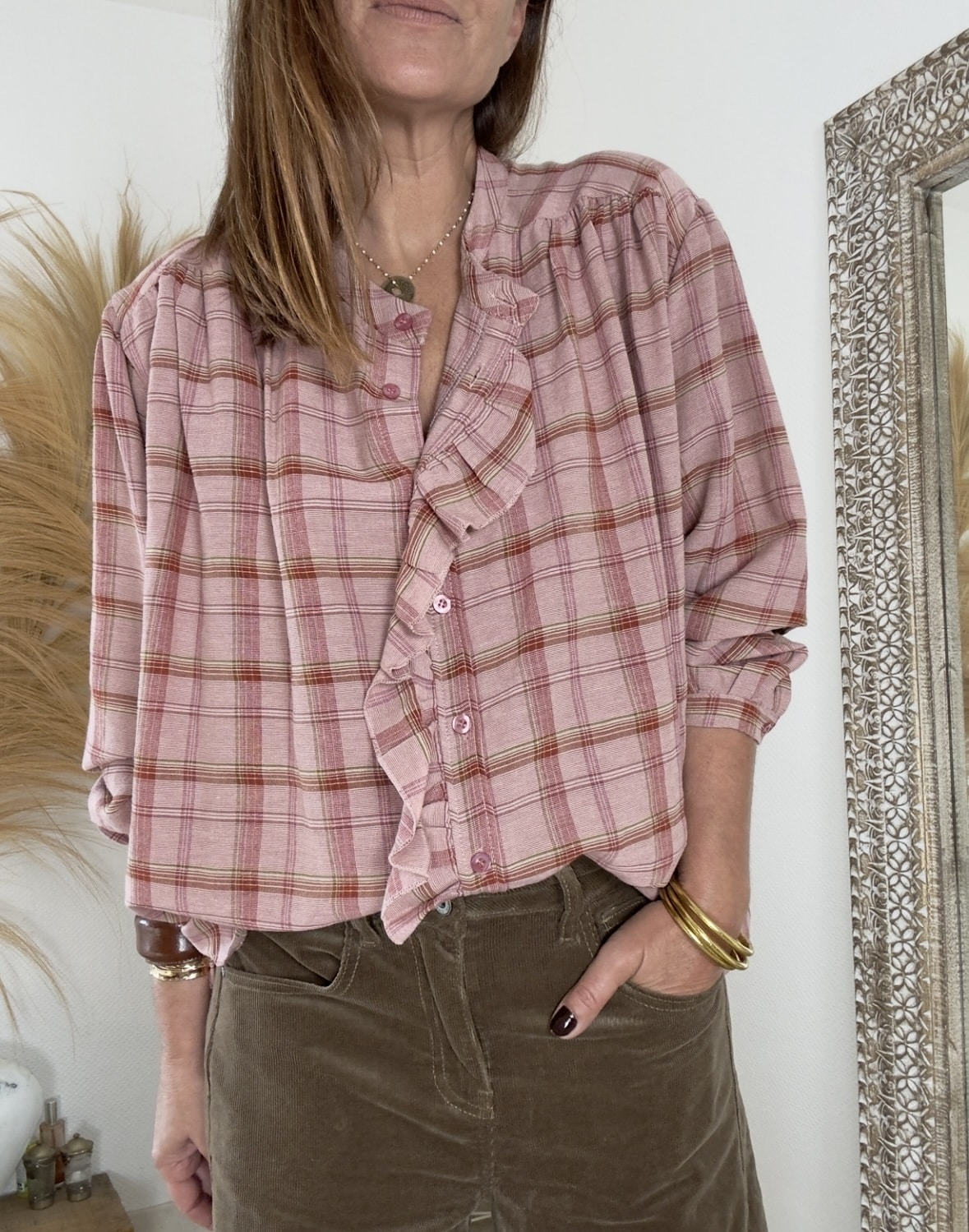 Élégance naturelle et féminité bohème chic La chemise RADIeUSE Johanna Paris séduit par son style fluide, doux et raffiné. Ses carreaux roses évoquent la tendresse et la lumière, parfaits pour adoucir les journées d’automne. Sa matière légère et fluide offre un tombé harmonieux et un confort agréable tout au long de la journée. La coupe ample apporte aisance et mouvement, tout en restant féminine et structurée. Le volant délicat qui longe toute la boutonnière ajoute une touche romantique et raffinée. Le col mao souligne le port de tête avec élégance, tandis que les manches longues fermées par un bouton assurent une allure soignée. De plus, de petites ouvertures sur les côtés apportent fluidité et modernité à la silhouette. Chaque détail a été pensé pour créer un équilibre entre simplicité et raffinement. Une matière fluide et agréable Grâce à sa composition en viscose, coton et polyamide, la chemise RADIeUSE combine douceur, souplesse et légèreté. La viscose assure un tombé fluide, le coton apporte respirabilité, et le polyamide garantit tenue et confort. Fabriquée en Italie, elle reflète un savoir-faire soigné et une qualité irréprochable. La matière est douce au toucher, légère sur la peau et facile à entretenir. Cette chemise devient rapidement un essentiel du dressing bohème chic. Des associations parfaites signées Les Marques de Lilo La chemise RADIeUSE s’accorde harmonieusement avec la jupe longue Thaïs prune pour une silhouette douce et féminine. Elle se marie aussi parfaitement avec la jupe Flora camel, créant un contraste lumineux et raffiné. Ces associations incarnent l’esprit Les Marques de Lilo : une mode fluide, naturelle et élégante. La chemise RADIeUSE exprime à merveille la féminité libre et poétique du style bohème chic. Une pièce légère, charmante et intemporelle à adopter sans hésiter.